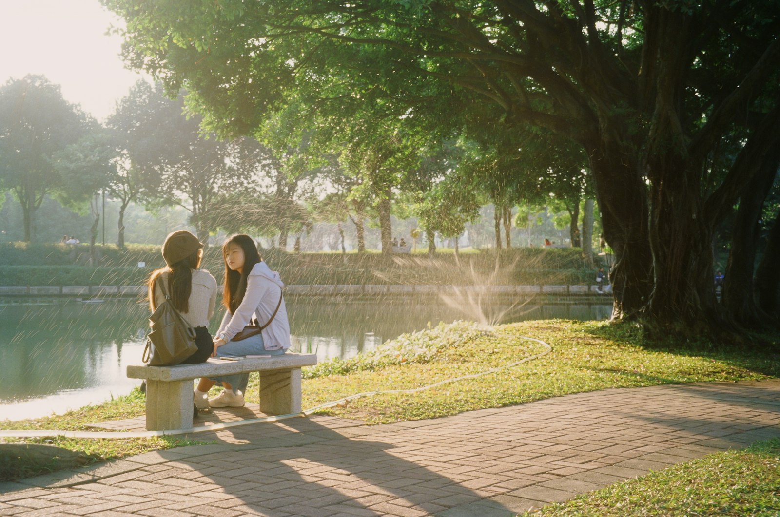 Two people sitting on a park bench by a lake, talking